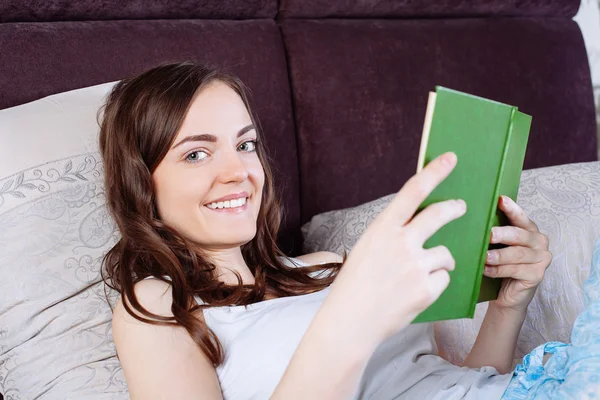 Mujer acostada en la cama mientras lee un libro — Foto de Stock