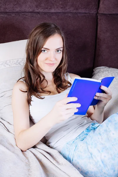 Mujer acostada en la cama mientras lee un libro — Foto de Stock