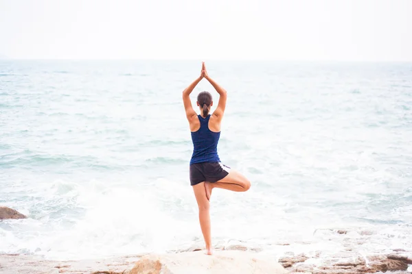 Young woman practicing tree yoga pose near the ocean — Stock Photo, Image