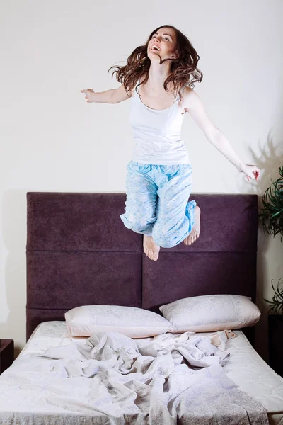 Glückliche junge Frau springt auf Bett — Stockfoto