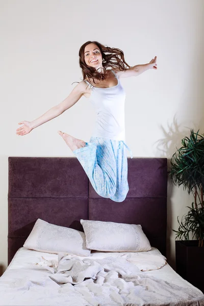 Glückliche junge Frau springt auf Bett — Stockfoto