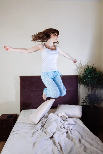 Glückliche junge Frau springt auf Bett — Stockfoto