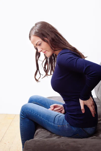 Jovem mulher sentada no sofá sofrendo de dor — Fotografia de Stock