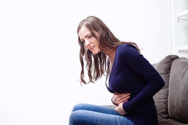 Giovane donna seduta sul divano che soffre di mal di stomaco — Foto Stock