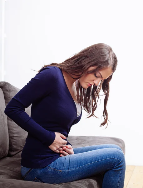 Молода жінка сидить на дивані страждає від болю в животі — стокове фото