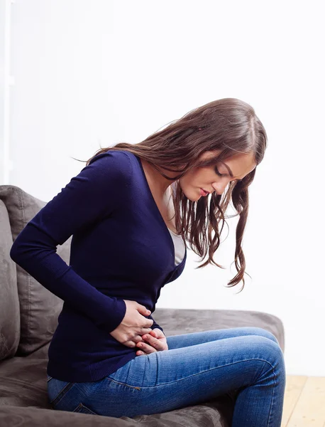 Junge Frau sitzt auf Sofa und leidet unter Bauchschmerzen — Stockfoto