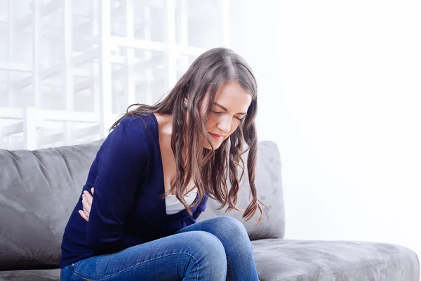 Jeune femme assise sur un canapé souffrant de maux de ventre — Photo