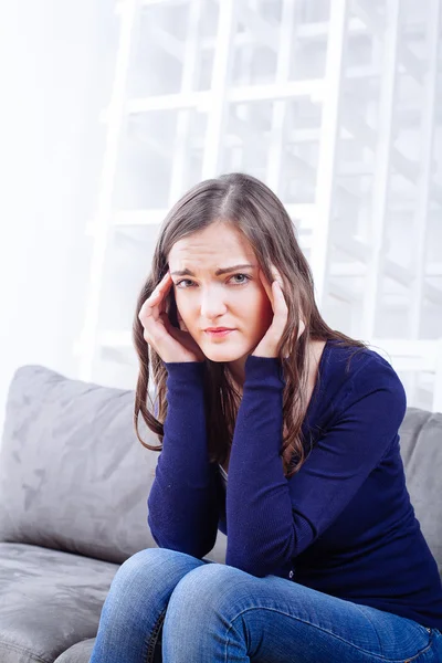 Mujer joven sentada en un sofá con dolor de cabeza migraña — Foto de Stock