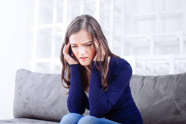 Mujer joven sentada en un sofá con dolor de cabeza migraña — Foto de Stock