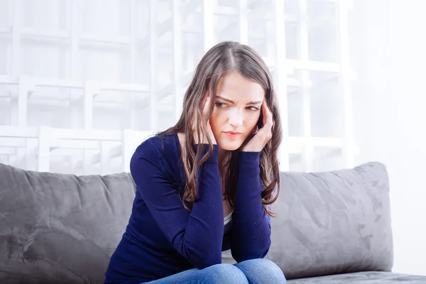 Mujer joven sentada en un sofá con dolor de cabeza migraña — Foto de Stock