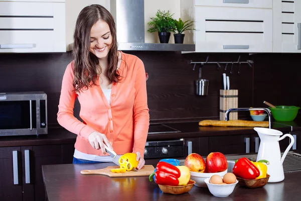 Mujer joven picando pimienta en la cocina — Foto de Stock