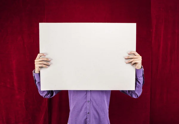 Hombre sosteniendo un cartel blanco sobre un fondo de terciopelo rojo — Foto de Stock