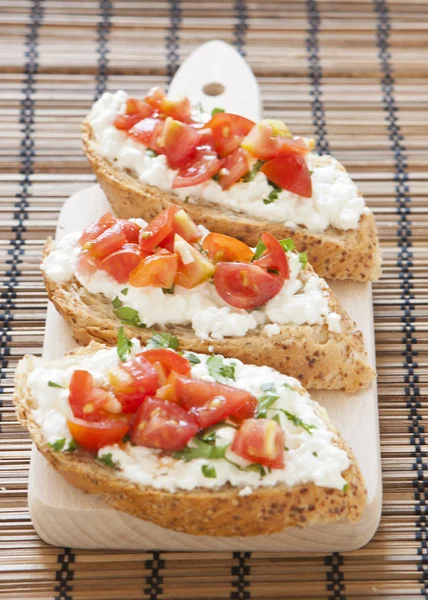 Crostini with cottage cheese, parsley and tomato on cutting boar — Stock Photo, Image