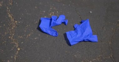 Kullanılmış plastik eldivenlerin bir mağazanın otoparkına dikkatsizce bırakılıp kaldırıldığı yakın çekim görüntüsü. 48fps yavaş çekim..  