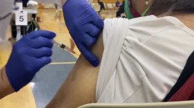 Yaşlı bir kadının spor salonundaki toplu aşılama kliniğinde ilk doz MODERNA COVID-19 aşısını alırken yakın çekim görüntüsü..  
