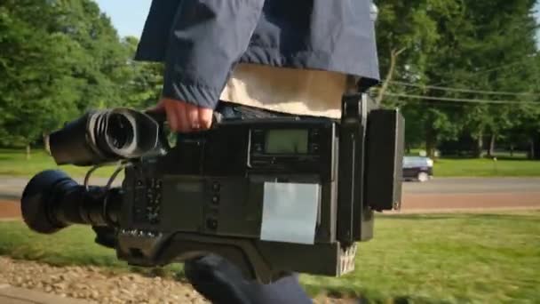 Um tiro de ângulo baixo de um cinegrafista levando sua câmera de vídeo para uma produção. Plano rastreável na câmera para colocação de um logotipo personalizado . — Vídeo de Stock