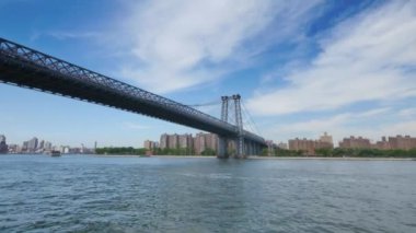 Uzakta Manhattan silueti ile Williamsburg Köprüsü altından geçen geniş bir çekim.