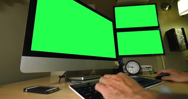 Ein Mann arbeitet an einem Computerarbeitsplatz. Monitore mit grünem Bildschirm für benutzerdefinierte Bilder. — Stockvideo