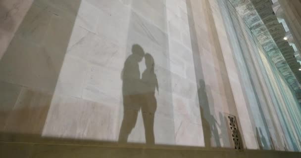 Two lovers kiss at the base of the Lincoln Memorial at night while their shadows fall on the marble walls. — Stock Video