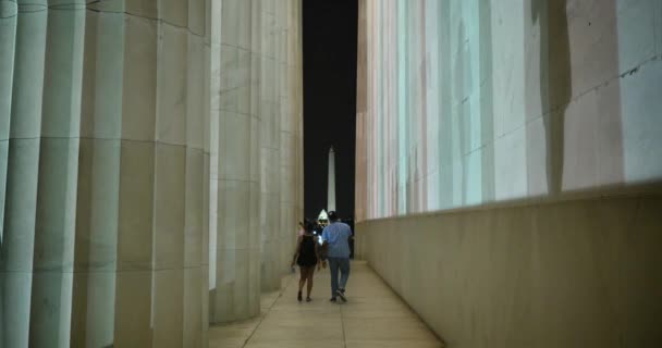 两人沿着侧林肯纪念堂在夜里走华盛顿纪念碑与国会大厦在背景中. — 图库视频影像