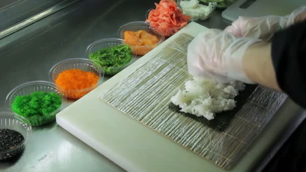 Cocinar haciendo rollos de sushi, esparciendo arroz sobre nori — Vídeos de Stock