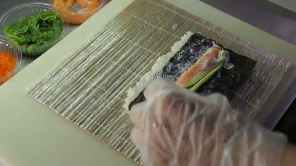Chef adicionando pepino e algas marinhas a rolos de sushi — Vídeo de Stock