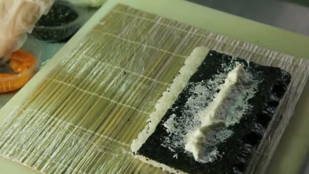 Шеф-кухар розтягує вершковий сир і кладе лосось під час приготування суші-роллів — стокове відео