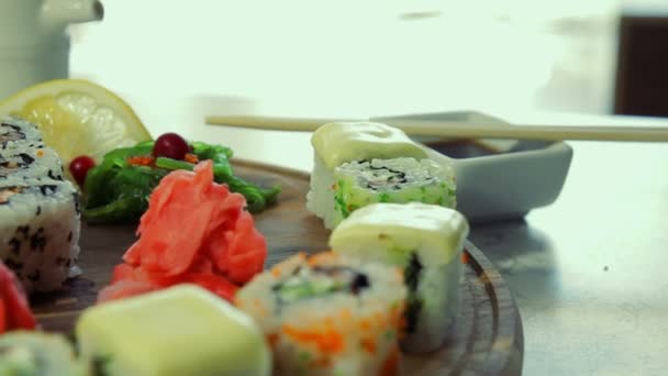 Dolly shot of delicious sushi rolls on wooden plate with wasabi and ginger — Stock Video