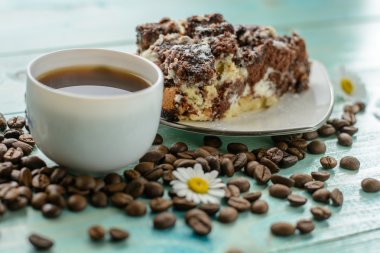 Fincan espresso, kahve çekirdekleri, papatya çiçek ve pasta ahşap turkuaz masa üzerinde