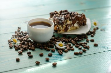 Fincan espresso, kahve çekirdekleri, papatya çiçek ve pasta ahşap turkuaz masa üzerinde