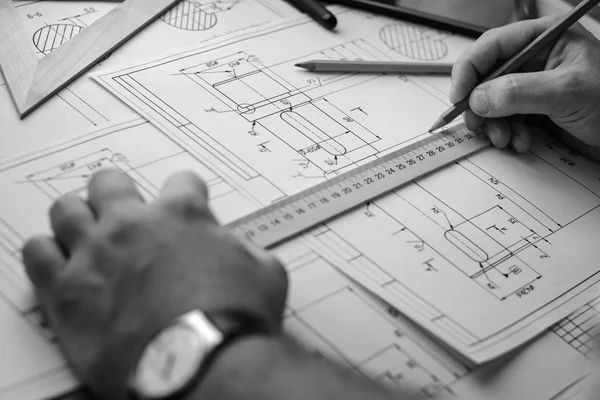 Man architect draws a plan, graph, design, geometric shapes by pencil on large sheet of paper at office desk. Soft focus.