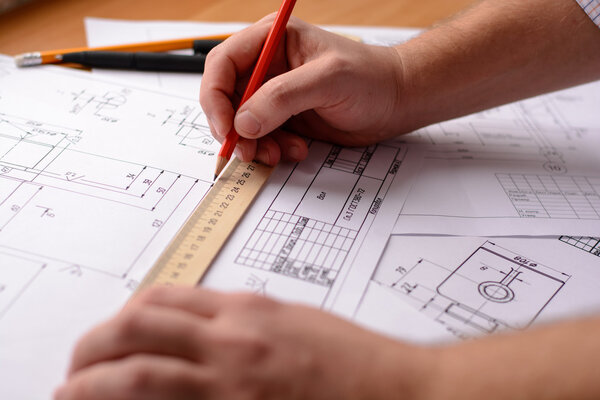 Girl architect draws a plan, graph, design, geometric shapes by pencil on large sheet of paper at office desk. Soft focus