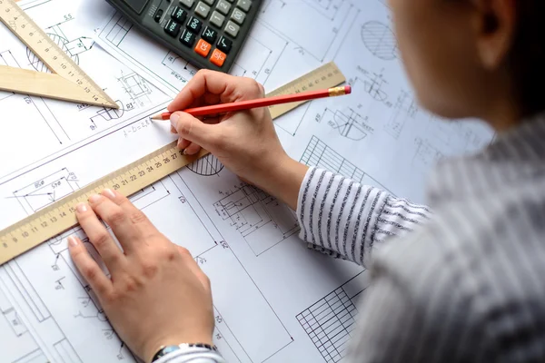 Girl architect dibuja un plano, gráfico, diseño, formas geométricas a lápiz en una gran hoja de papel en el escritorio de la oficina. Enfoque suave — Foto de Stock