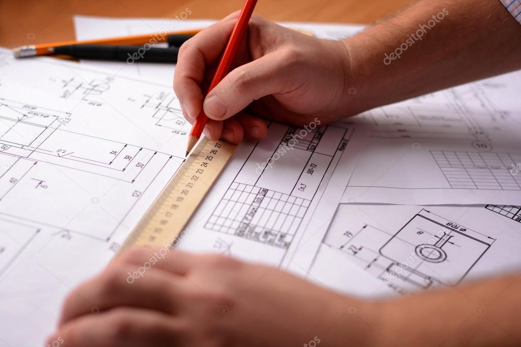 Man architect draws a plan, graph, design, geometric shapes by pencil on large sheet of paper at office desk. Soft focus.