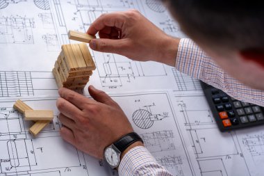 Adam mimar Ofis Masası, kağıt üzerine büyük kalem tarafından bir plan, grafik, tasarım, geometrik şekiller çizer ve ahşap bloklar (çubuk evden model oluşturur)
