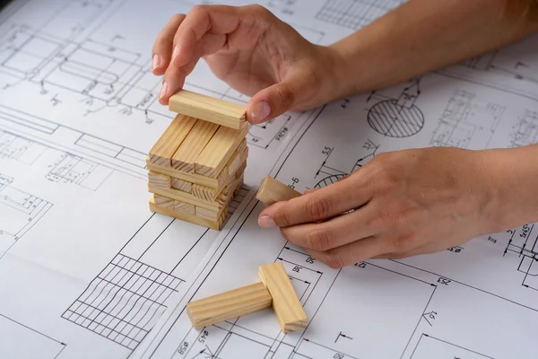 Man arkitekt ritar en plan, Graf, design, geometriska former av penna på stora pappersark på skrivbord och bygger modell hus från träklossar (barer) — Stockfoto