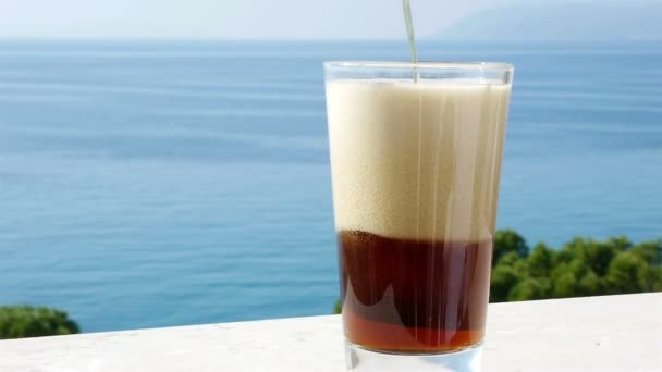 Verser la bière noire dans un verre avec la mer en arrière-plan — Video