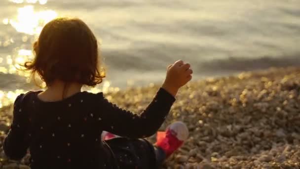 Menina pequena na praia jogando pedras no mar — Vídeo de Stock