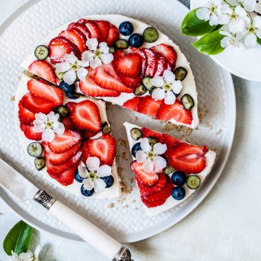 Çilekli ve yaban mersinsiz peynirli kek Bahar çiçekleriyle süslenmiş, kare şeklinde.