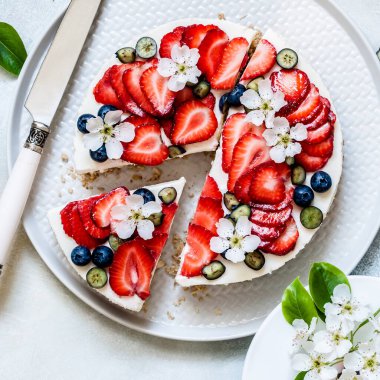 Çilekli ve yaban mersinsiz peynirli kek Bahar çiçekleriyle süslenmiş, kare şeklinde.