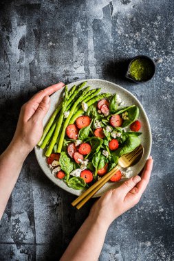 Bir tabak çilek, ıspanak, kuşkonmaz ve Pesto soslu Feta salatası tutan eller, metnin için kopyalama alanı