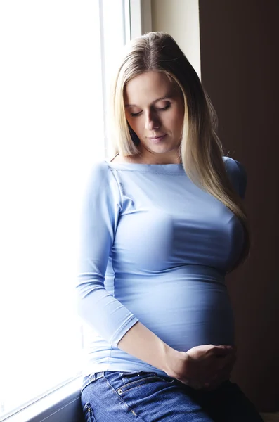 Zwangere vrouw zitten door het venster — Stockfoto