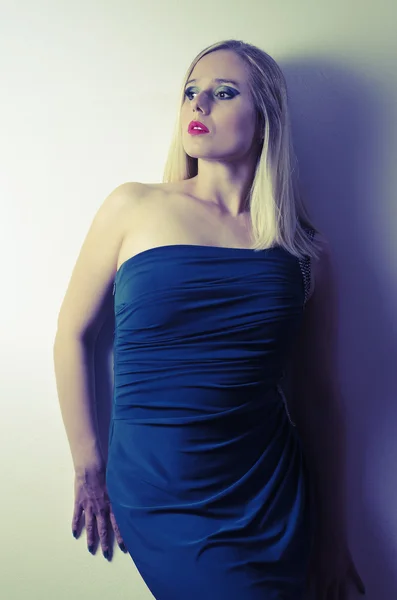 Femme blonde posant dans une robe bleue appuyée contre un mur blanc — Photo