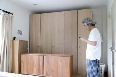 Yatak odasında akıllı telefon kullanan kıdemli Asyalı adam..