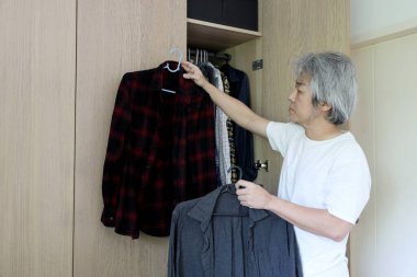 Üst düzey Asyalı adam yatak odasında kıyafet seçiyor..