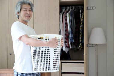 Çamaşır yıkamak için çamaşır sepeti taşıyan Asyalı adam..