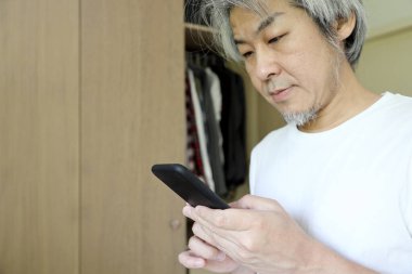 Odada akıllı telefon kullanan Asyalı adam..