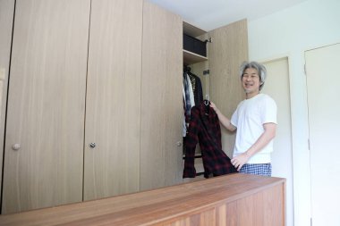 Üst düzey Asyalı adam yatak odasında kıyafet seçiyor..