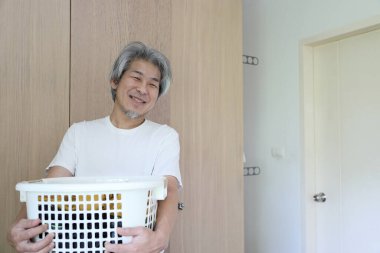 Çamaşır yıkamak için çamaşır sepeti taşıyan Asyalı adam..