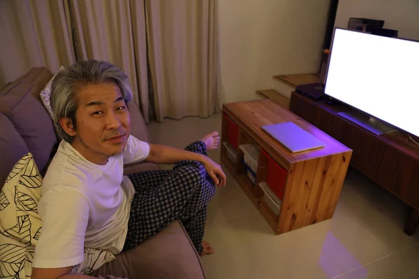 Den Ældre Asiatiske Mand Sidder Sofaen Ser Fjernsyn Kameraet Fokuserer - Stock-foto